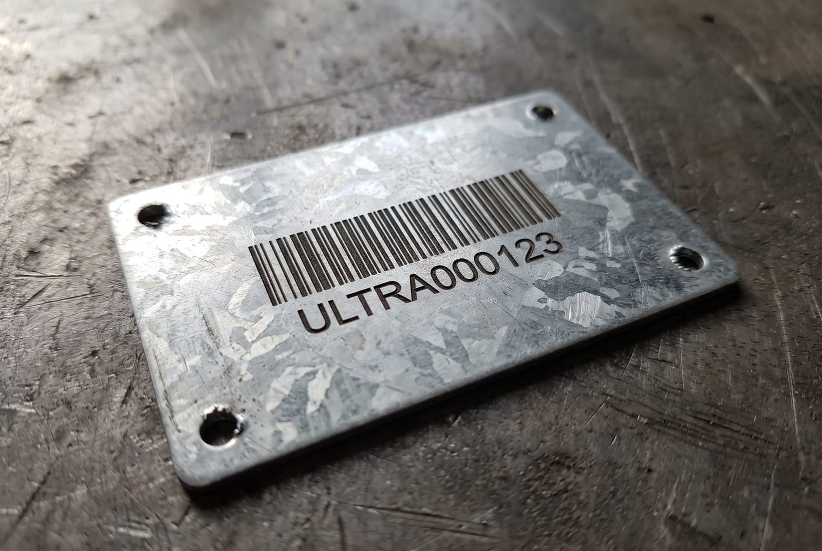 Оцинкованная бирка крупным планом: штрих-код и номер ULTRA000123 лазерной гравировкой в металле